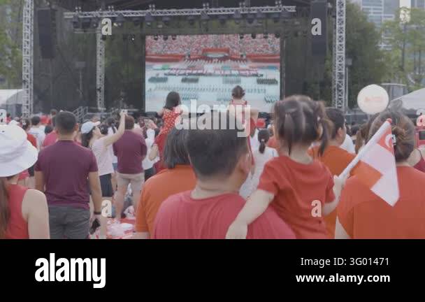 Spectators wearing red shirts and holding small Singapore flags watch ...