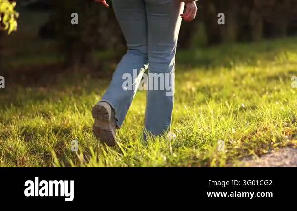 Rear close view of a womans legs in light blue jeans and boots walking ...