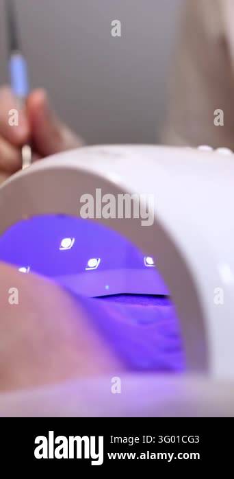 Close-up of a clients foot inside a UV LED nail lamp glowing purple ...