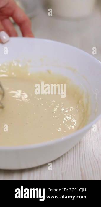 Close up of a metal whisk moving through a glossy dough mixture in a ...
