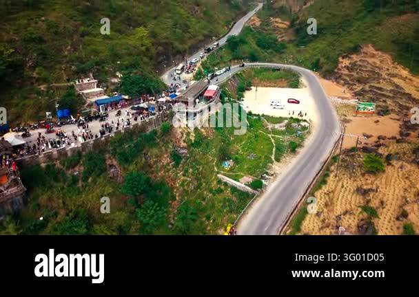 An aerial view follows a winding road past a village and fields through ...