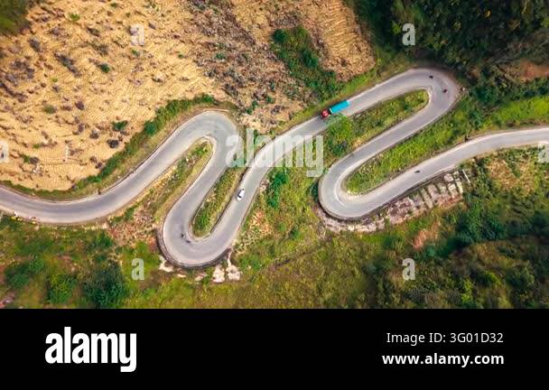 An aerial view follows vehicles along a winding mountain road through ...