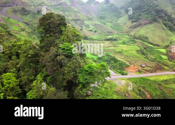An aerial view follows a winding road through green mountain valleys ...