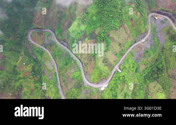 An aerial view follows a winding road through green mountain terrain on ...