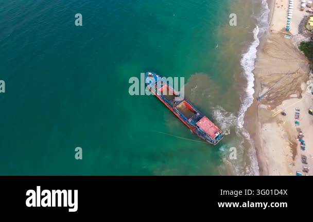 A cargo boat moves through coastal water toward a sandy shore near Hoi ...