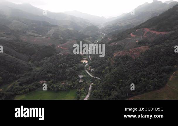 An aerial view follows a winding road through forested mountain valleys ...