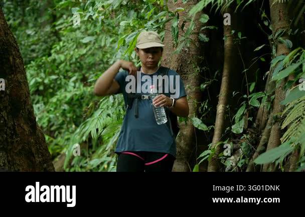 Asian female hiker drinking water from bottle taking a break in lush ...