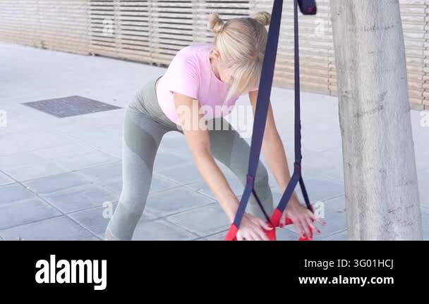 Fit woman working out with resistance bands attached to a tree during ...
