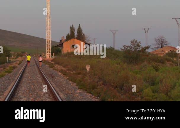Two people walk beside a railway at dusk through misty countryside ...