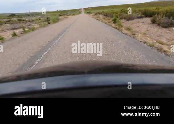 A road-level view from a moving vehicle on a weathered two-lane highway ...