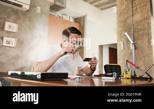 Electronics Componenets Mature Asian man looks at and considers circuit board details with ...