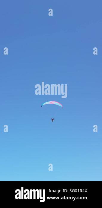 Vertical view of paraglider soaring under colorful canopy high in clear ...