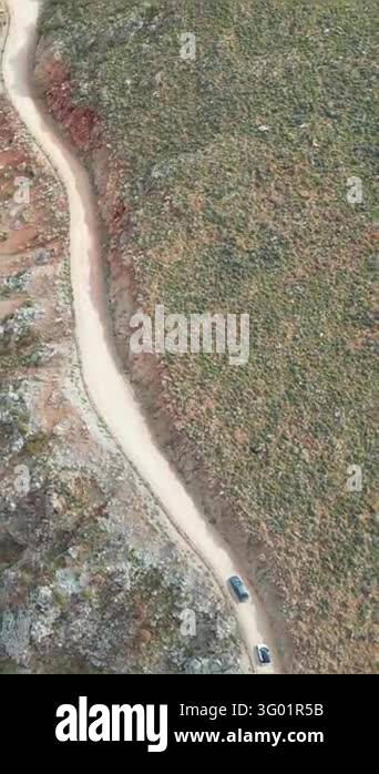 Vertical aerial top down view of cars driving along winding unpaved ...
