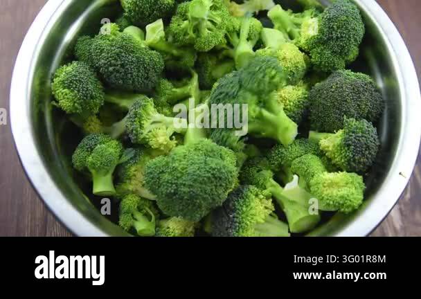 Close up view of raw fresh green broccoli florets in metal bowl and on ...