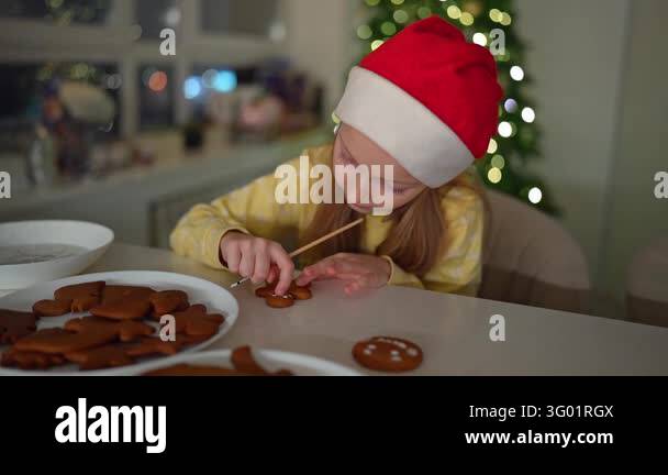 Girl wearing red hat and yellow sweater spreads icing on gingerbread ...