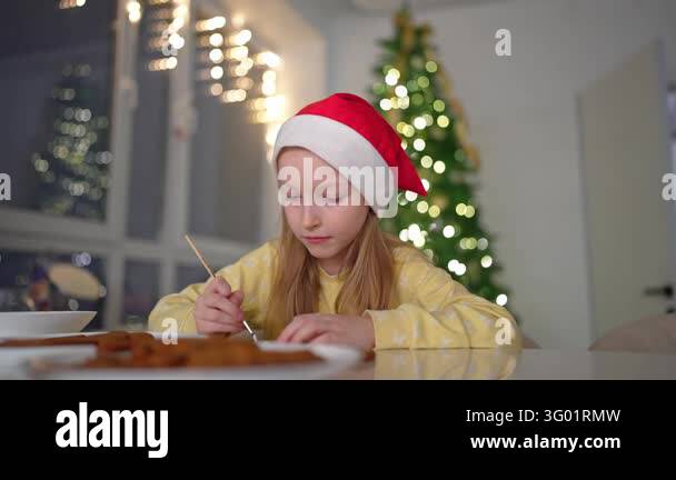 Girl wearing red hat and yellow sweater spreads icing on gingerbread ...