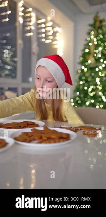Girl wearing red hat and yellow sweater spreads icing on gingerbread ...