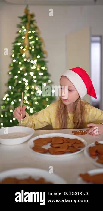 Girl wearing red hat and yellow sweater spreads icing on gingerbread ...