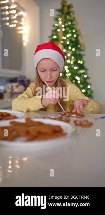 Girl wearing red hat and yellow sweater spreads icing on gingerbread ...