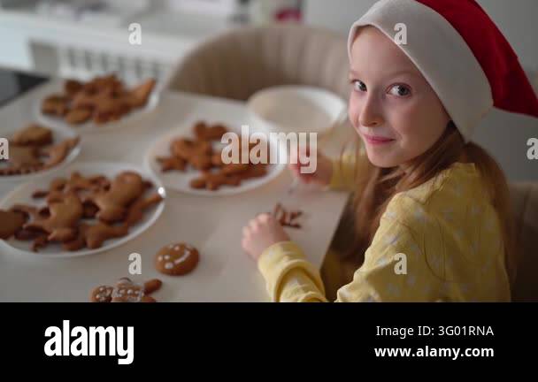 Young girl in Santa hat and yellow pajamas smiles while piping icing ...