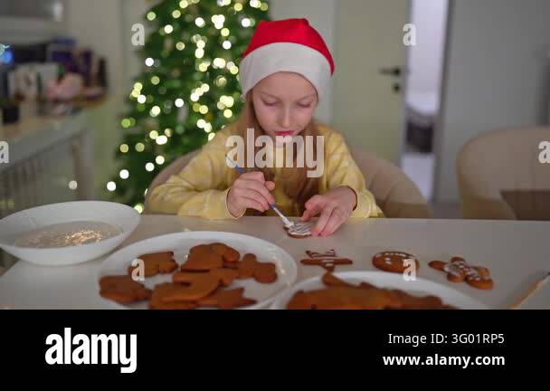 Girl in Santa hat carefully places iced gingerbread cookies on glossy ...