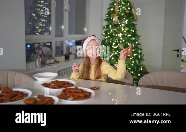 Girl wearing red hat and yellow sweater spreads icing on gingerbread ...