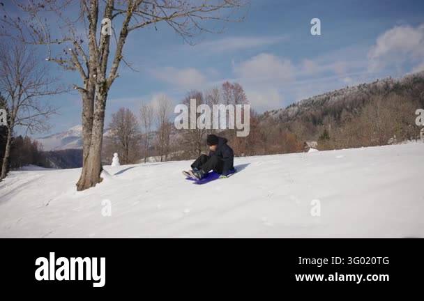 Ecxitment Boy riding a plastic sled down a snowy hill, enjoying the excitement ...
