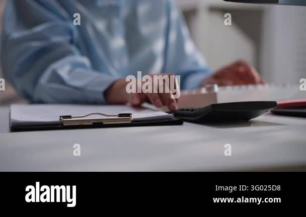 Office worker pressing a calculator beside printed financial paperwork ...