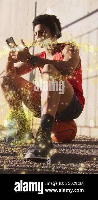 Vertical video: Athlete sitting on basketball scrolling phone during ...