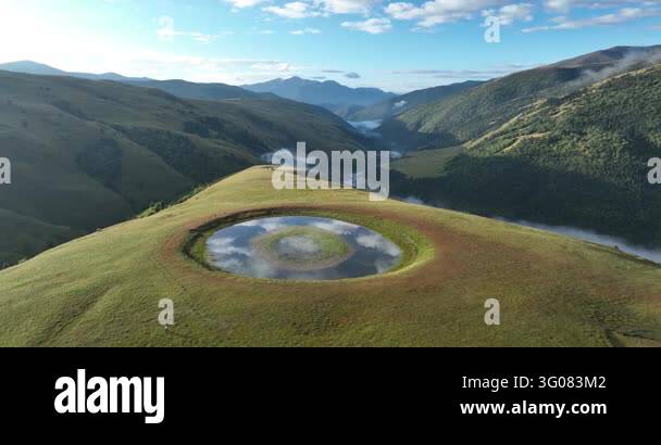 Aerial drone footage of a circular pond on a grassy mountain ridge ...