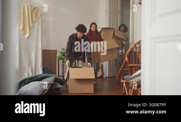 Friends carry large cardboard boxes into an apartment as they begin the ...
