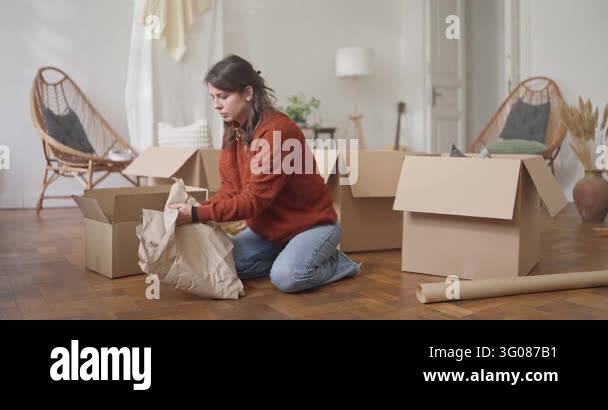 Concentrated girl sitting on floor putting dishes in wrapping paper ...