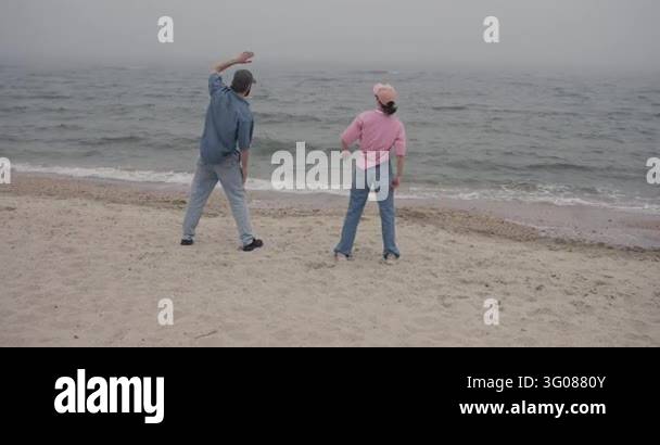 Two adults stretching together on foggy sandy beach, side view of backs ...