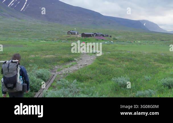 A solitary hiker walks along the Kungsleden trail in a vast, lush ...