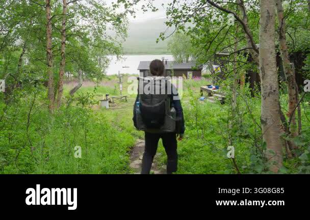 A hiker with a backpack walks on a forest trail towards the remote ...