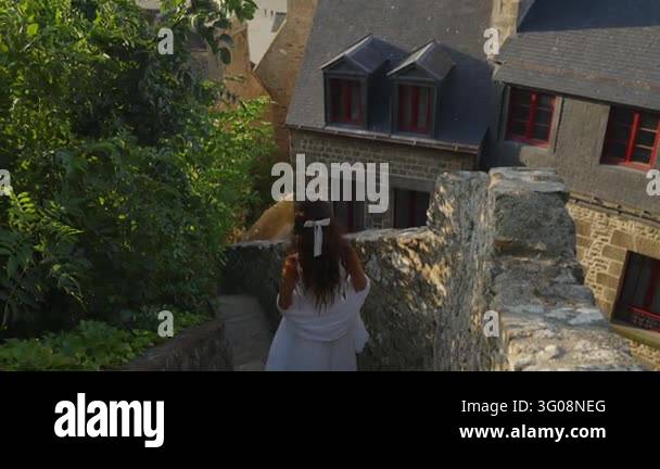 France Tree A woman in a flowing white dress walks down narrow medieval stone ...