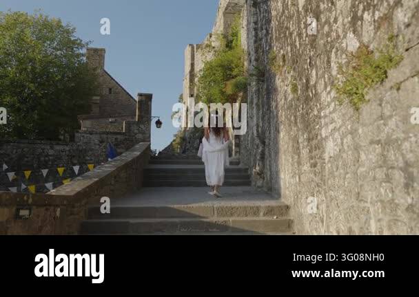 France Tree Seen from behind a woman in a flowing white dress walks up medieval ...