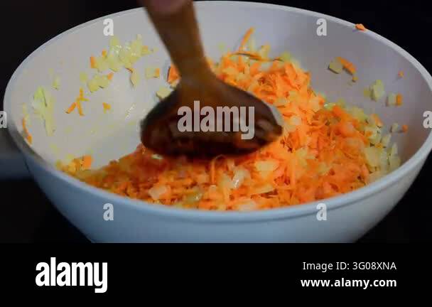 Kitchen Cook Using Spoon a cook using a wooden spoon to stir and saut shredded orange carrots ...