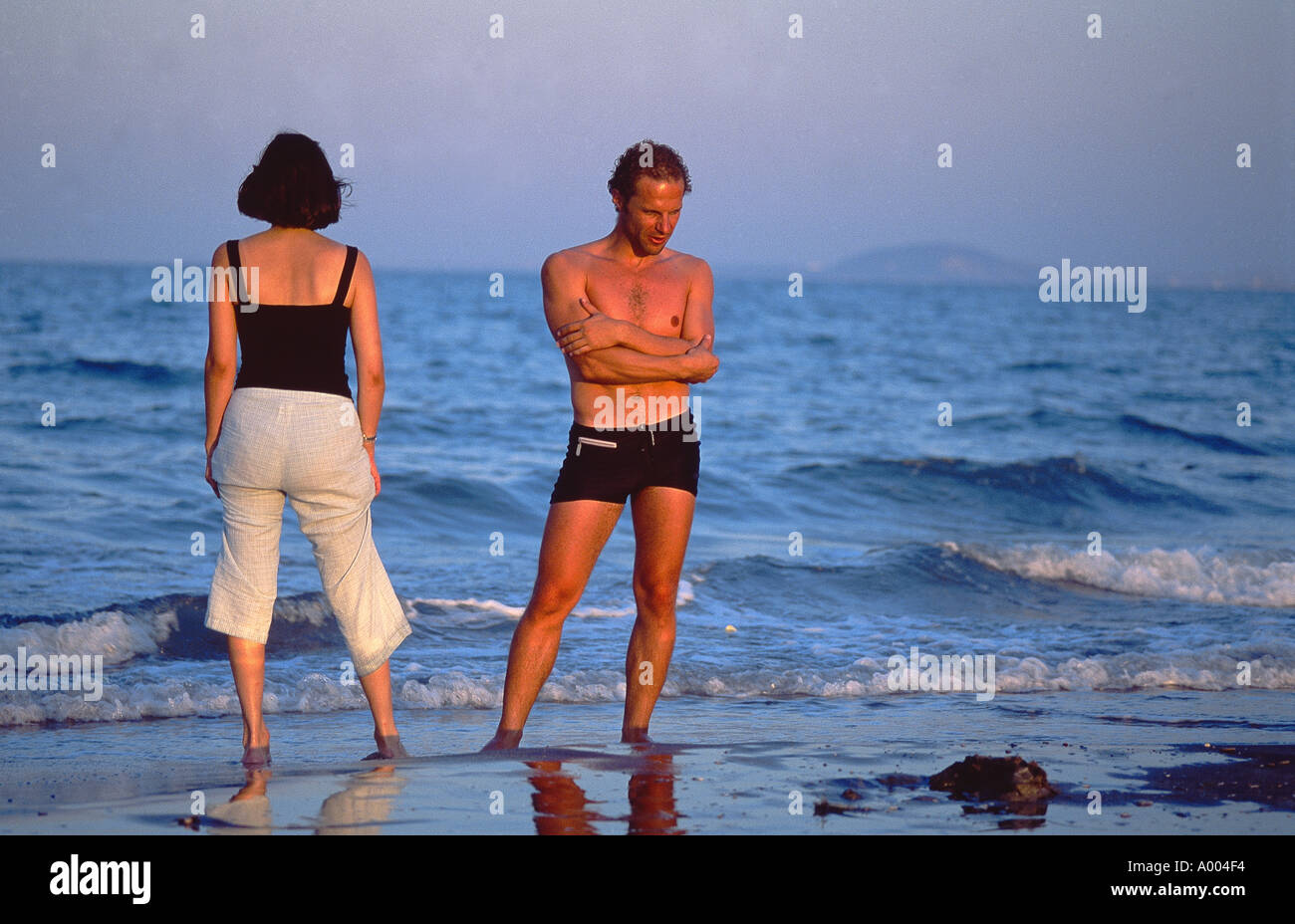 Couple on holiday- standing on the beach looking in different directions Stock Photo