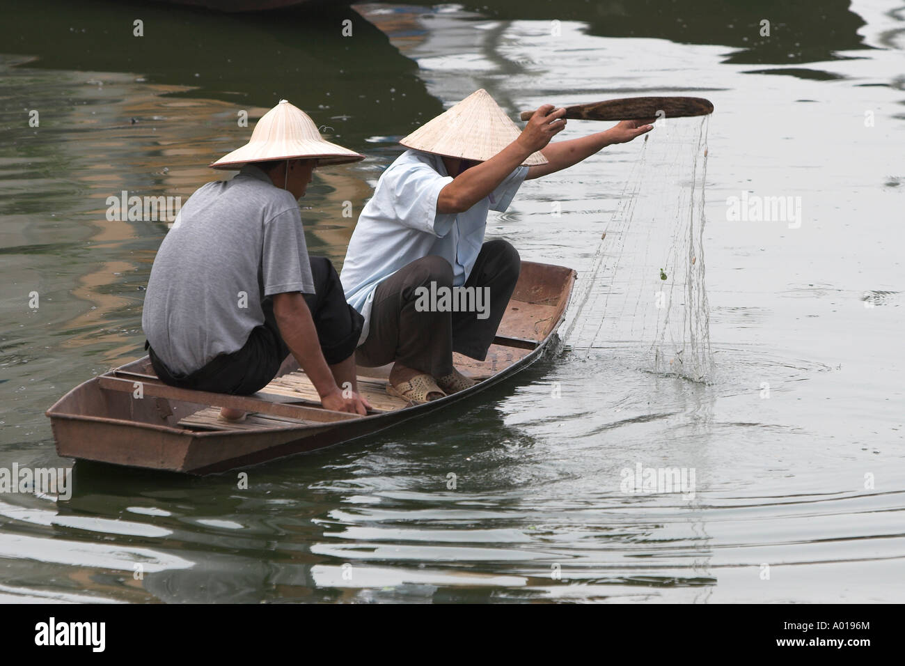 Two men fishing from small boat with net and paddle Yen River