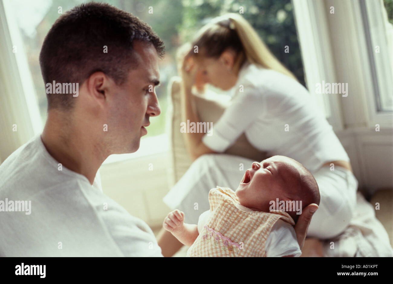 man holding a young baby as the mother looks depressed in  the background Stock Photo