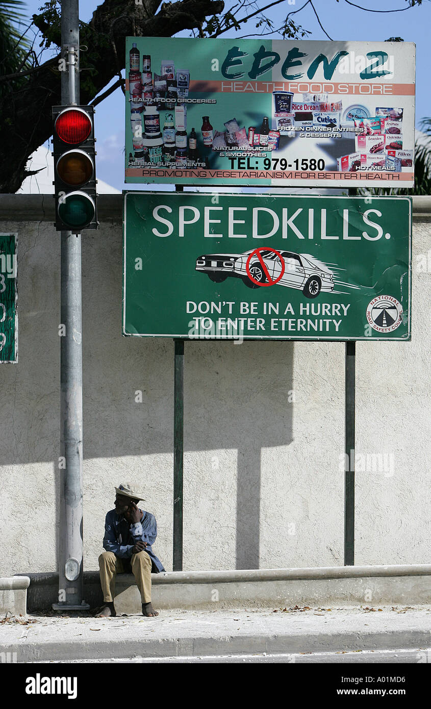 A man sits on the sidewalk under traffic safety signs at an