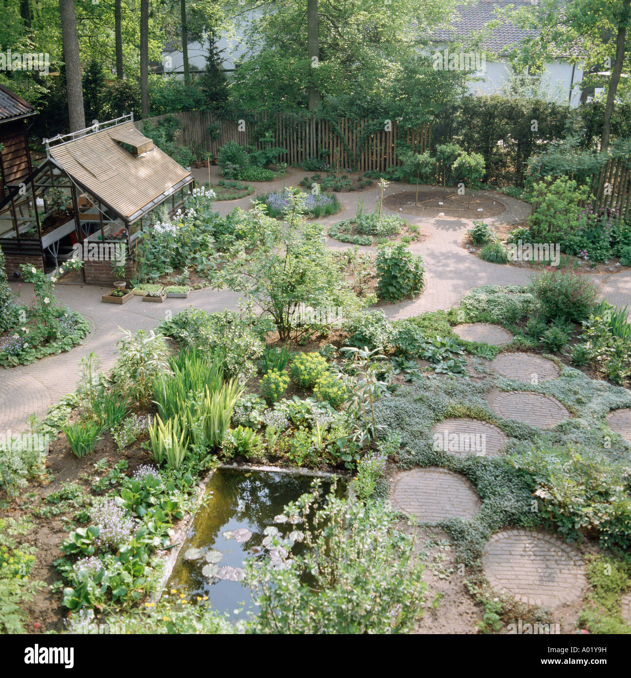 Birdseye view of greenhouse in garden with small pond and paved paths