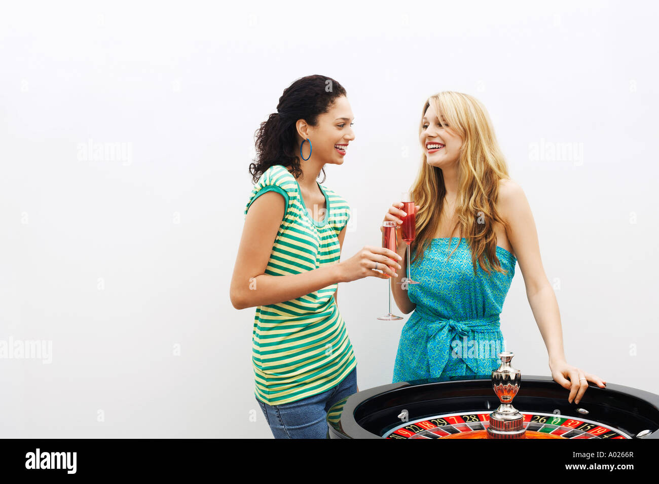 Two young women drinking cocktails by roulette wheel Stock Photo