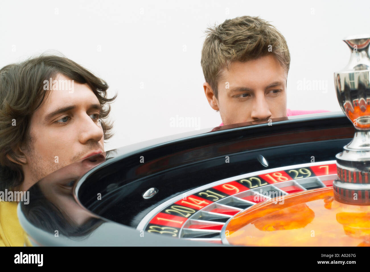 Two hopeful  young men crouching at roulette wheel watching spin, close up Stock Photo