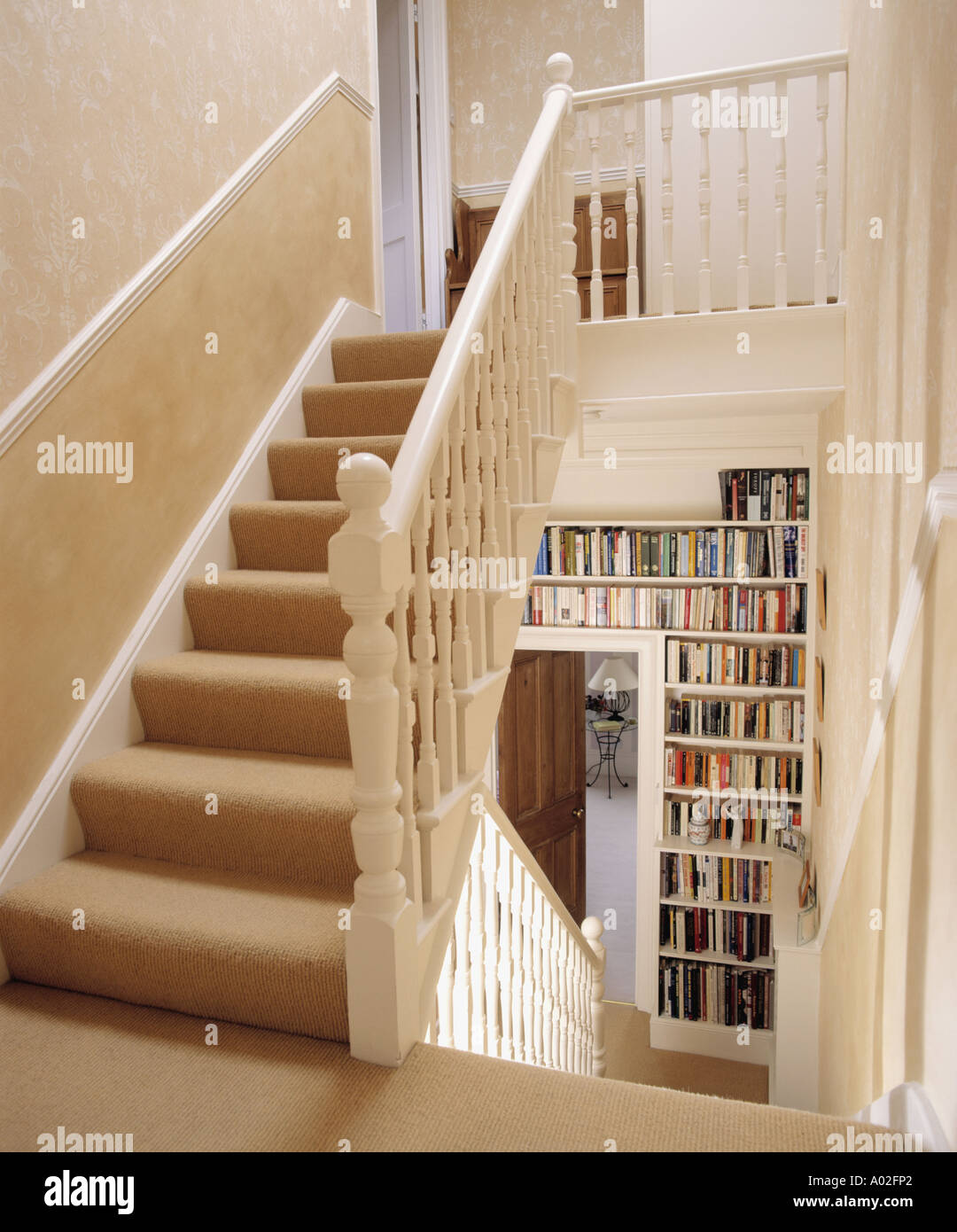 Cream carpet on landing stairs above hall with fitted bookshelves Stock