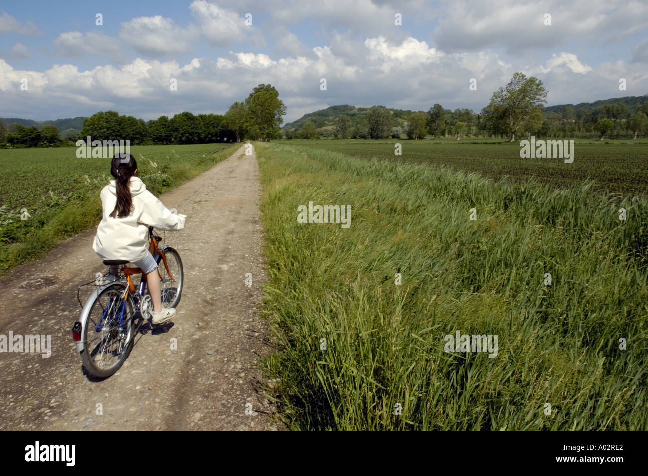 Girl cycling through fields in the countryside along a rural track Stock Photo