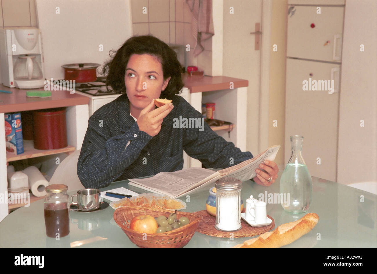 Woman eating breakfast reading newspaper and glancing at clock Stock Photo