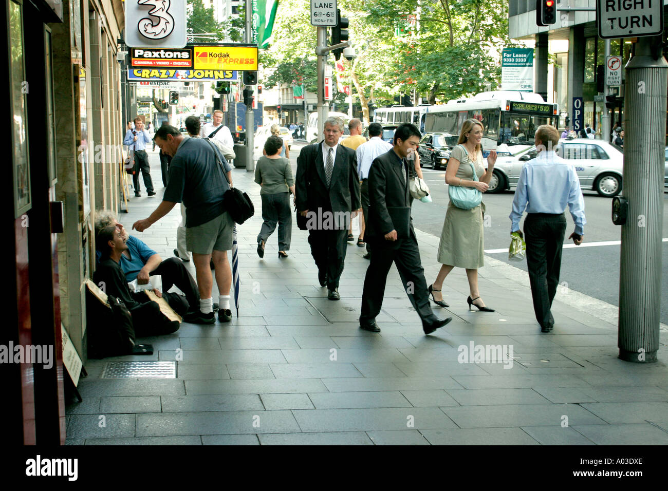 A man abuses a beggar in George street Sydney whilst passersby wait for traffic lights Stock Photo