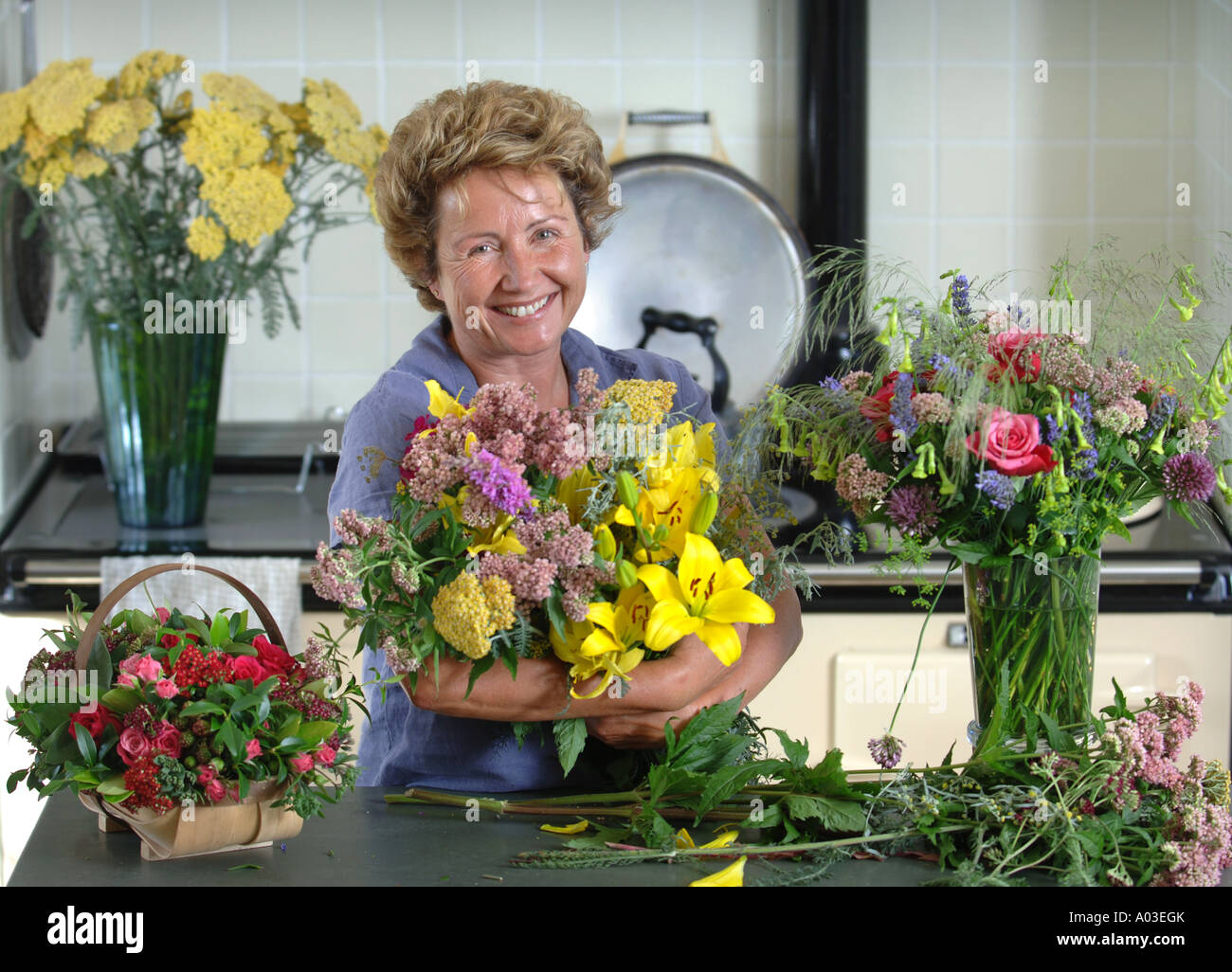 A FEMALE GARDENER WITH CUT FLOWERS INCLUDING LILIES IN A COUNTRY KITCHEN UK Stock Photo